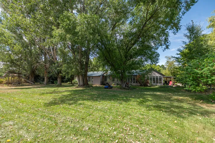 Expansive lawn with mature trees and a single-story residence featuring a sunroom with multiple windows
