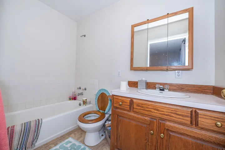 White bathtub with white tile surround, wood-finish vanity with an integrated sink, and a wood-frame medicine cabinet