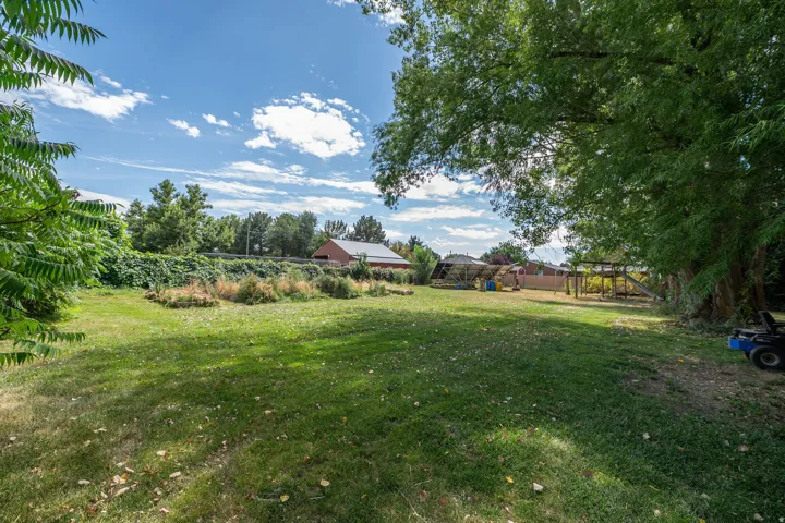 Expansive grassy yard with mature trees providing shade and a distant barn structure