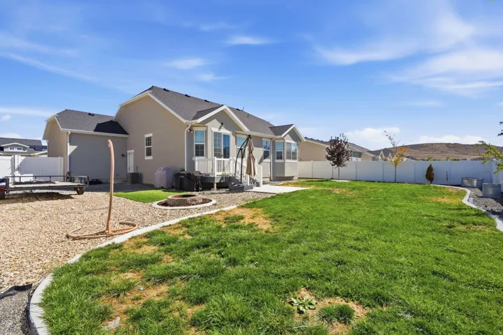Expansive backyard featuring a green lawn, gravel landscaping, a built-in fire pit, and a white privacy fence