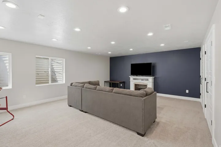Recessed ceiling lighting, white trim detail, window with blinds, blue accent wall, and built-in white fireplace mantel