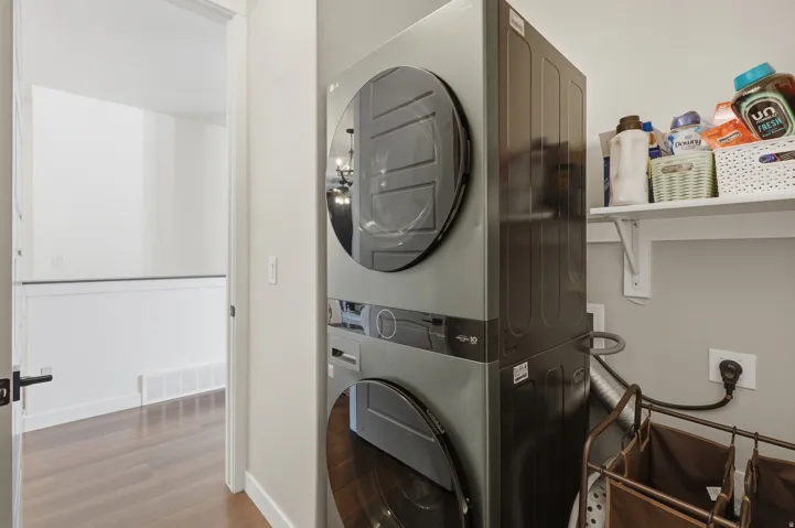 Laundry area with stacked appliances, open shelving, and wood-finish flooring