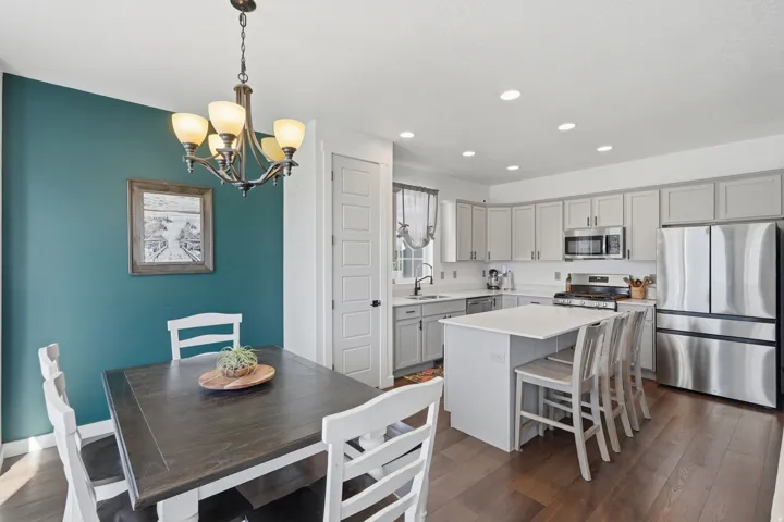 Open-concept kitchen and dining area featuring dark wood-finish flooring, recessed lighting, and a white kitchen island with counter seating