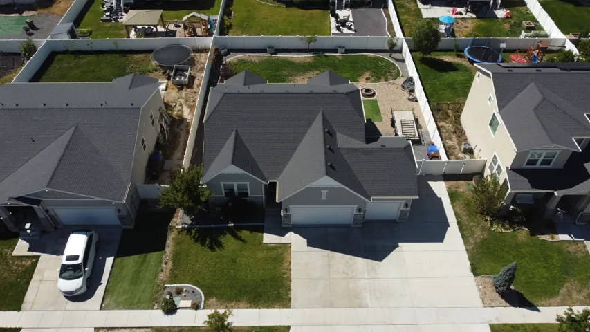 Gray exterior with a dark shingle roof, attached garage, concrete driveway, and front lawn