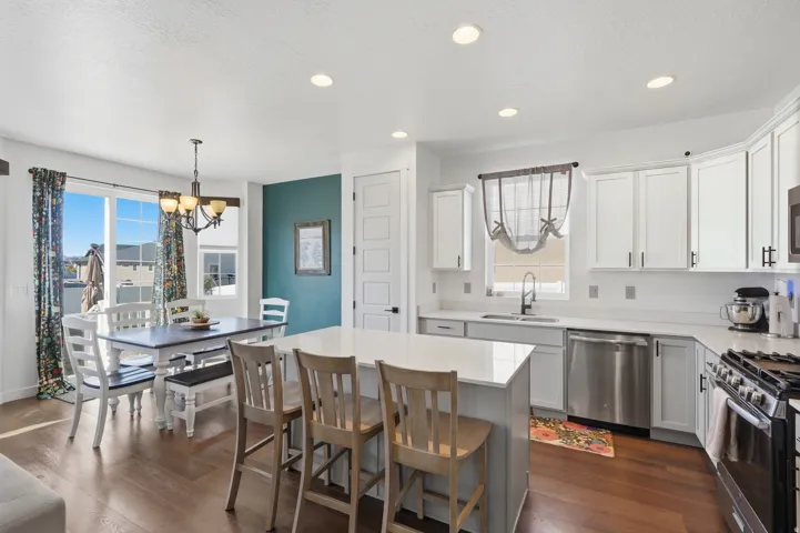 Open-concept kitchen and dining area featuring a central island with countertop seating, stainless steel appliances, white cabinetry, and wood-finish flooring