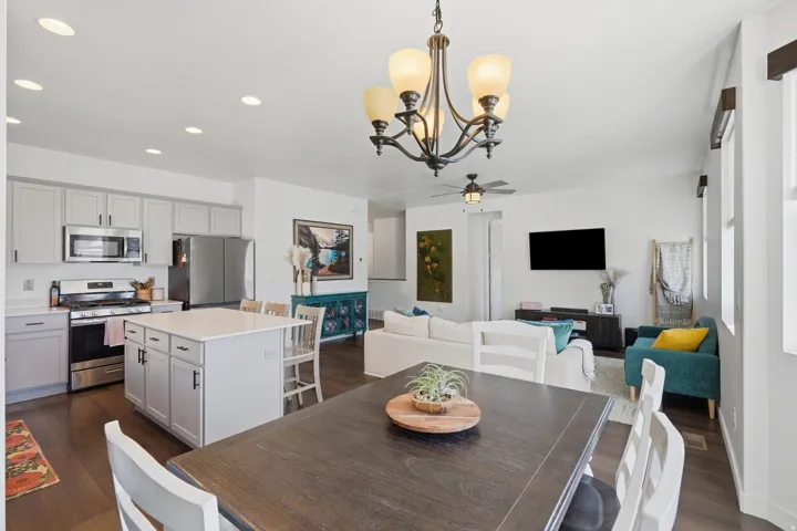Open-concept living space featuring a kitchen with light-colored cabinetry and stainless steel appliances, a center island with seating, a dining area, and a living area with wood-finish flooring