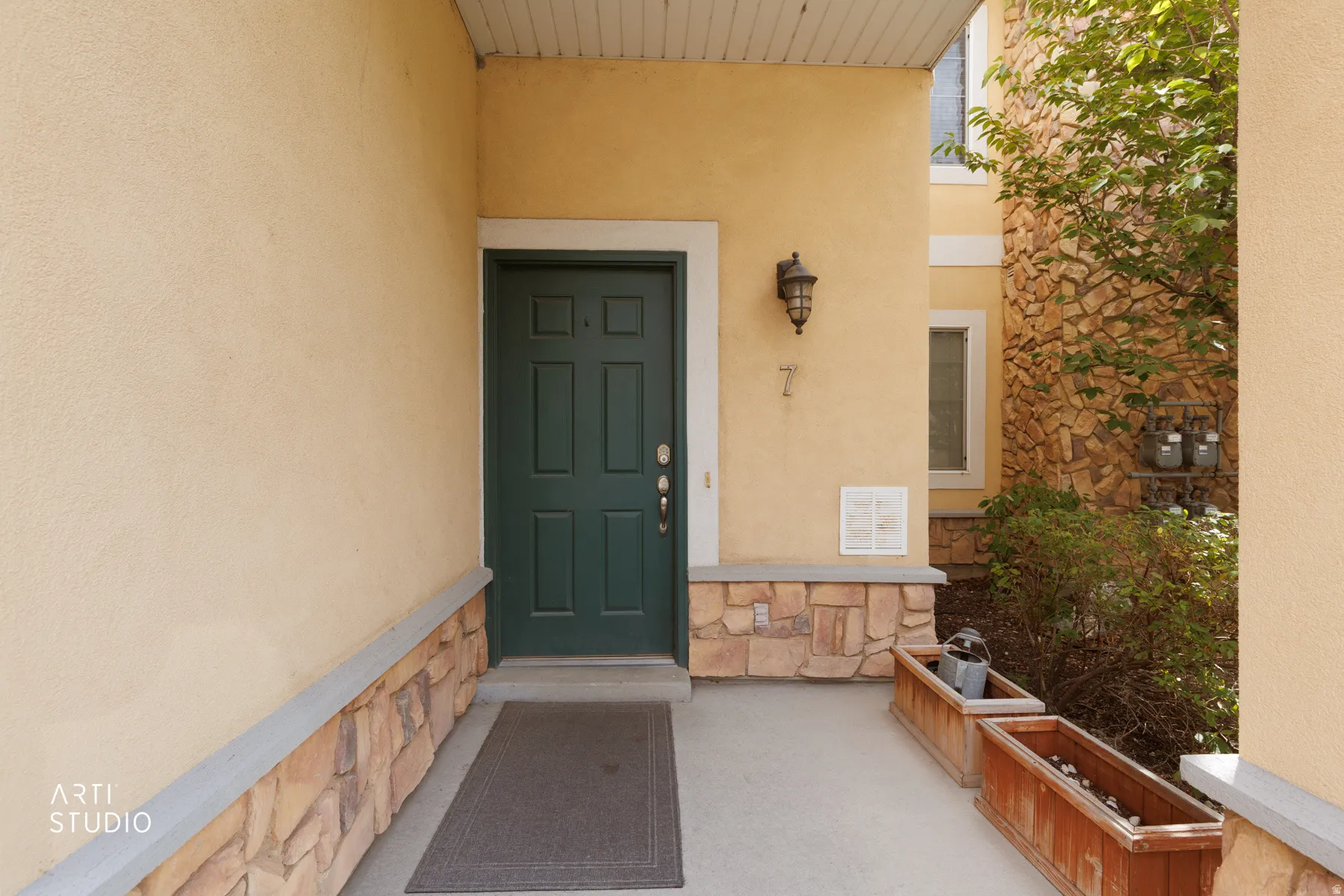 Stucco exterior with stone veneer accents, six-panel entry door, and outdoor wall sconce