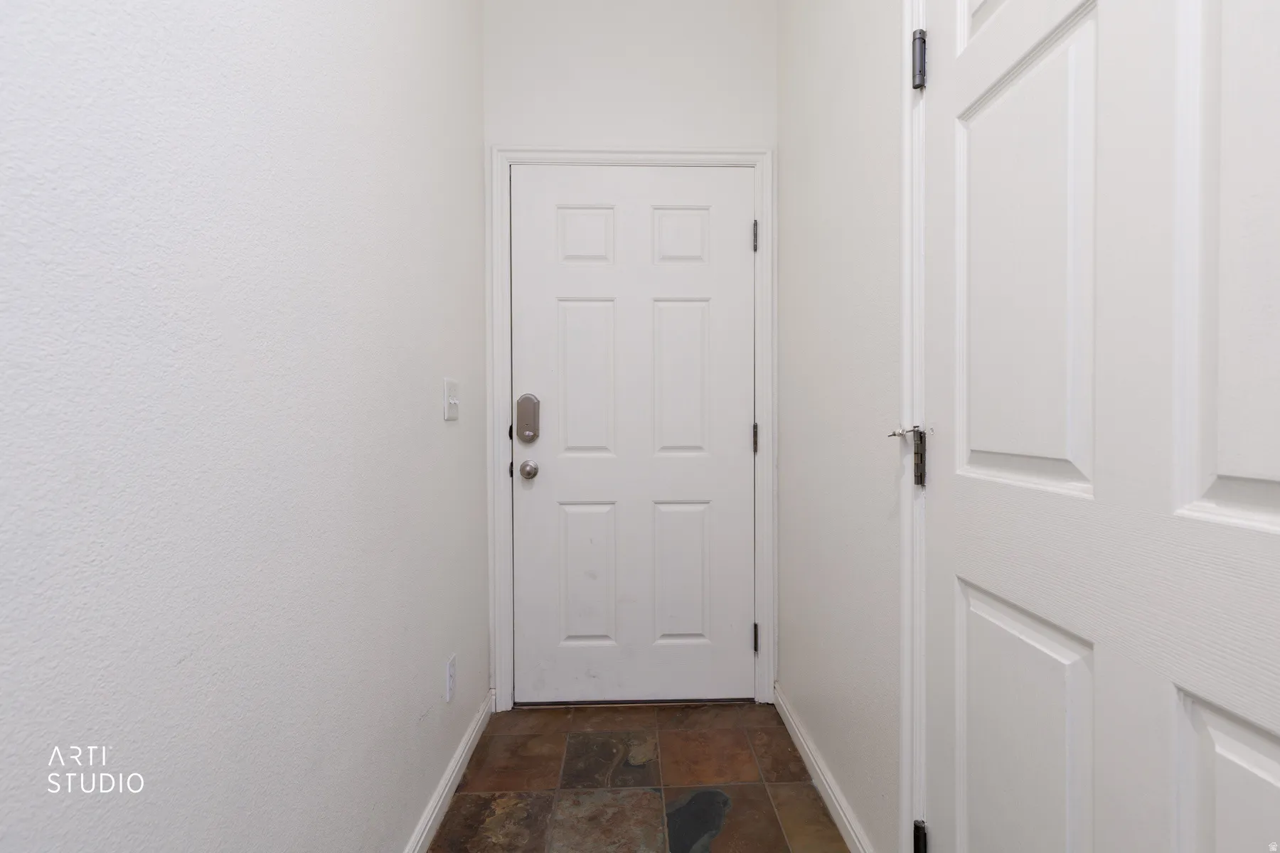 White paneled door with brushed nickel hardware and a digital key lock, set against white textured walls, and dark tone tile flooring