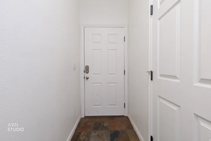 White paneled door with brushed nickel hardware and a digital key lock, set against white textured walls, and dark tone tile flooring