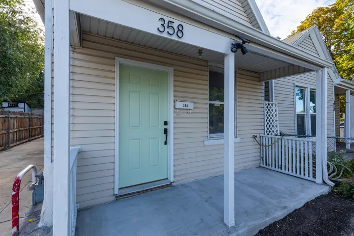 Covered concrete porch with a light green entry door and vinyl siding