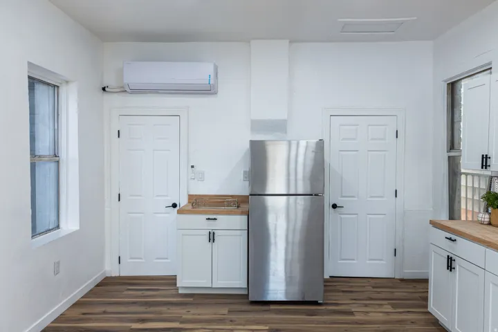 Wood-finish flooring, white cabinetry with matte black hardware, stainless steel refrigerator, light wood-finish countertops, and white paneled doors