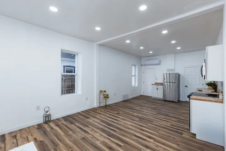 Open-concept living area featuring wood-finish flooring, recessed lighting, white walls, and a kitchen area with white cabinetry and stainless steel appliances