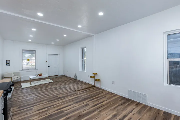 Wood-finish flooring, white walls, recessed ceiling lighting, multiple windows, and a paneled entry door