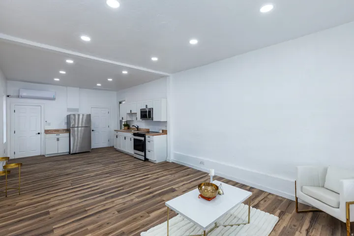 Open-concept room featuring wood-finish flooring, recessed lighting, and a kitchen area with white cabinetry and stainless steel appliances