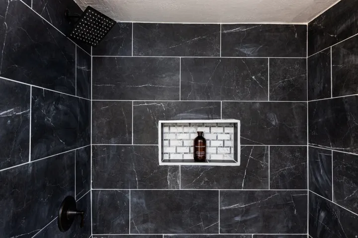 Black tiled shower with a black rainfall showerhead, black shower control, and a tiled shower niche with subway tile accent