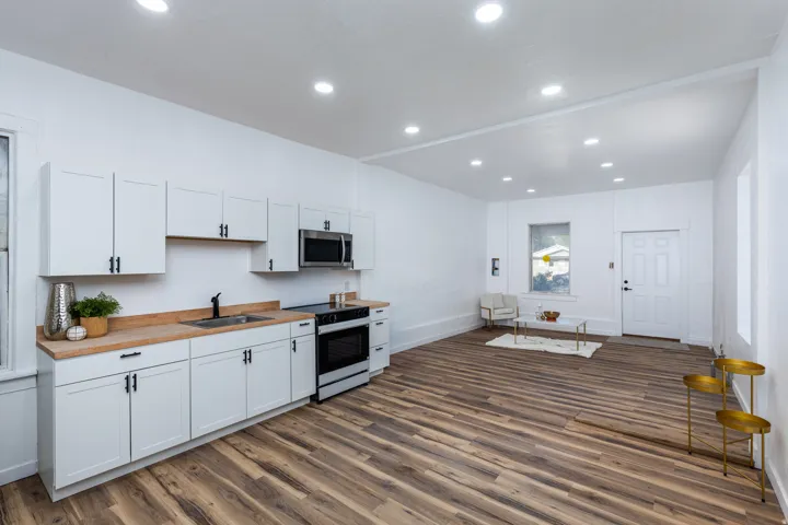 Open-concept living space with wood-finish flooring, recessed lighting, white cabinetry with black hardware, wood-finish countertops, and stainless steel appliances
