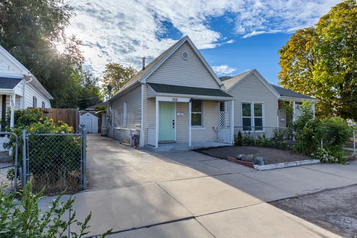 Siding exterior with a covered porch, an arched gable, a concrete driveway, and a front yard with mature landscaping