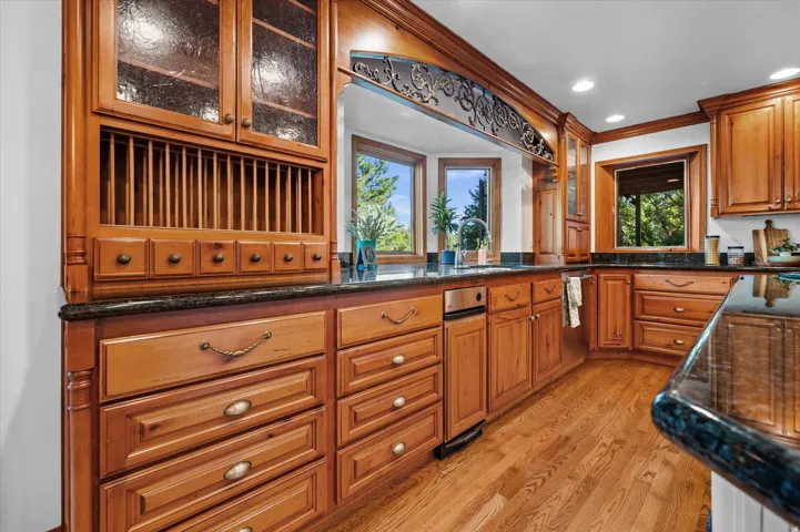 Wood-finish cabinetry with decorative hardware, dark stone countertops, wood-finish flooring, recessed lighting, and a bay window