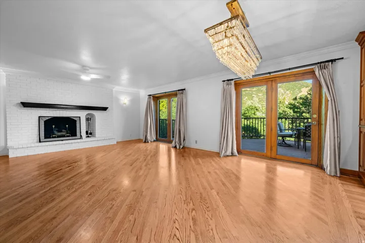 Hardwood flooring, white brick fireplace with mantel, double glass patio doors, and a crystal chandelier
