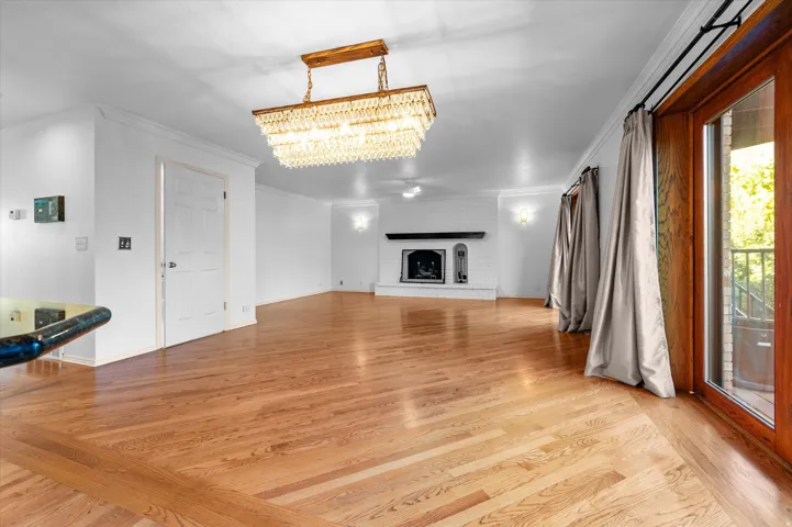 Hardwood flooring with a perimeter inlay, elegant crystal chandelier, white brick fireplace with a dark wood mantel, built-in wall sconces, and a glass-paneled wooden exterior door