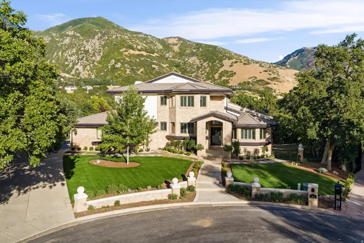 Stately residence featuring a brick and stucco exterior, arched entry, multiple bay windows, manicured front lawns, and mature trees