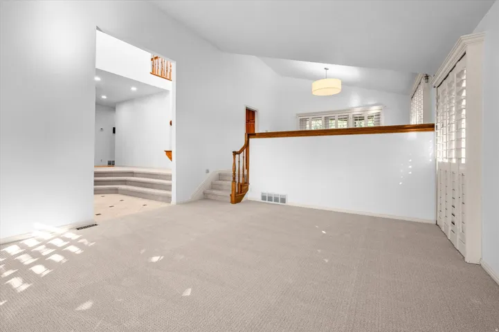 Carpeted living area with vaulted ceiling and contemporary drum pendant lighting for formal dining or flex space