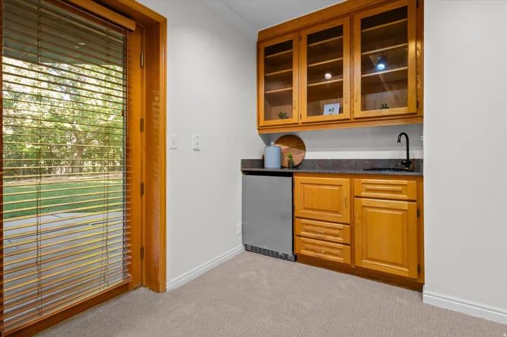 Built-in wet bar featuring wood cabinetry, glass-front upper cabinets, a stone countertop, and an undermount sink with a black faucet