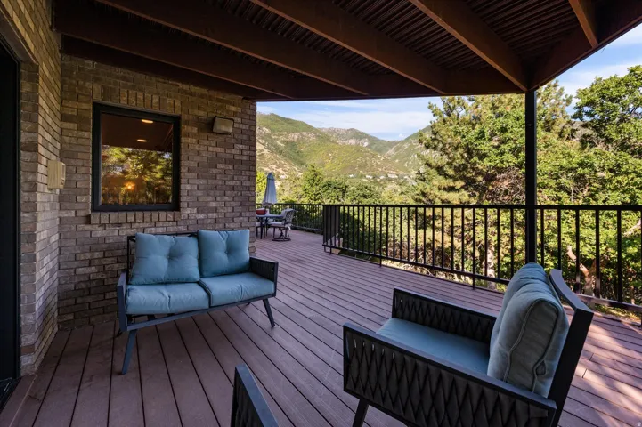 Spacious covered deck featuring composite decking, a black metal railing, and a brick exterior wall
