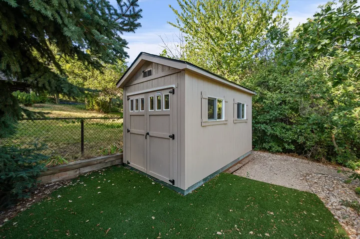 Exterior storage shed with a gable roof, double doors, and two side windows