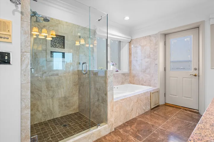 Glass-enclosed shower with stone tile surround and mosaic accent with door to private balcony