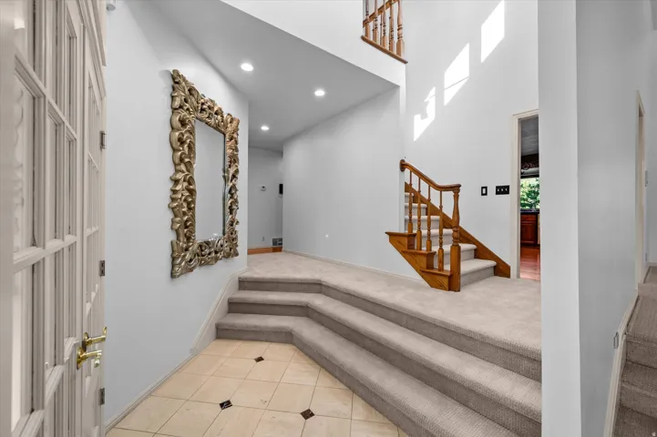 Tiled entry flooring, wood staircase with carpeted treads, recessed lighting, and a two-story ceiling