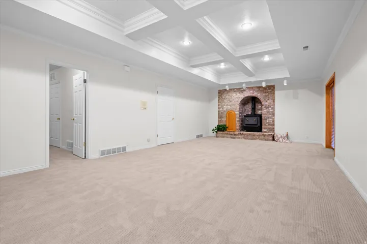 Spacious room featuring a coffered ceiling with recessed lighting, brick-faced fireplace with a wood-burning stove, and neutral-toned carpeting