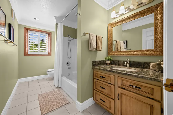 Hardwood vanity with a stone countertop, a large framed mirror, and a full bathtub with shower