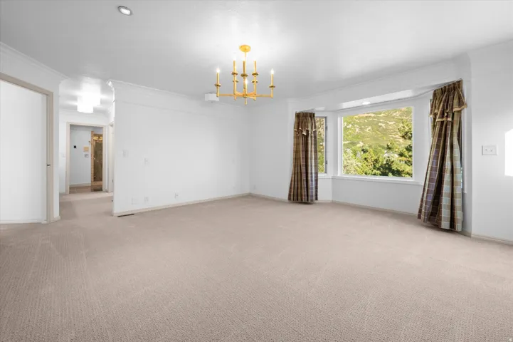 Spacious room featuring a bay window, crown molding, a brass-tone chandelier, and recessed lighting