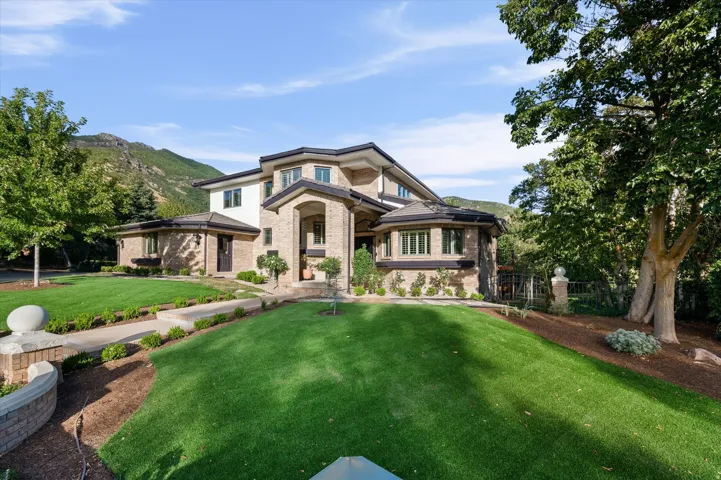 Multi-level residence featuring brick and light stucco, a prominent arched entry, and a manicured lawn with mature trees