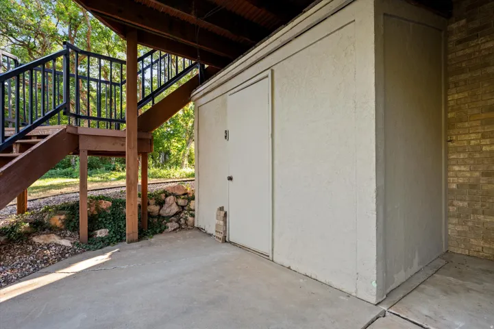 Concrete patio with stucco storage unit, natural wood stairs, and dark metal railing