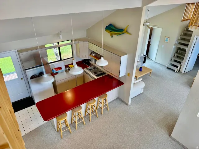 Vaulted ceiling, built-in kitchen cabinetry, red countertop island, built-in electric range, and carpeted stairs