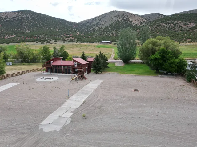 Red-roofed structure with an expansive deck, concrete patio area with fire pit, and surrounding mountains