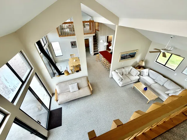 Vaulted ceiling with exposed beams, multiple large windows, and a lofted area with wood railings