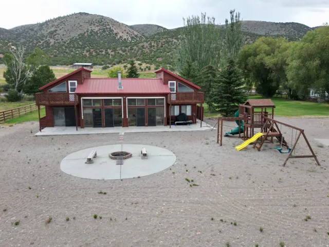Red metal roof, expansive rear patio, upper-level balcony, circular fire pit with seating, and a large outdoor playset