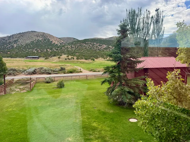 Expansive green lawn, fenced perimeter, distant mountainous terrain, red siding structure with metal roof, mature trees