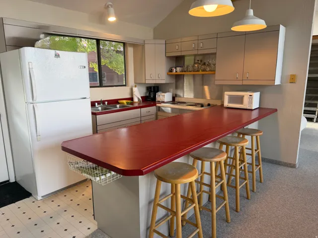 Kitchen featuring a red countertop with integrated casual dining, light-toned cabinetry, stainless steel double-basin sink, and a large window