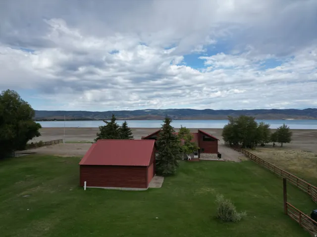 Waterfront property featuring a red metal roof, expansive green lawn, and a wooden fence