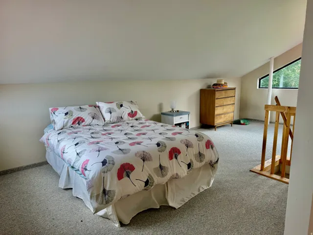 Sloped ceiling with recessed lighting, light-toned carpeting, and a window with a trapezoidal shape
