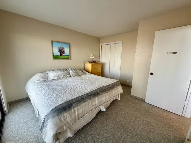 Neutral wall paint, textured ceiling, light-toned carpet flooring, white bi-fold closet doors, and a white solid door with dark hardware
