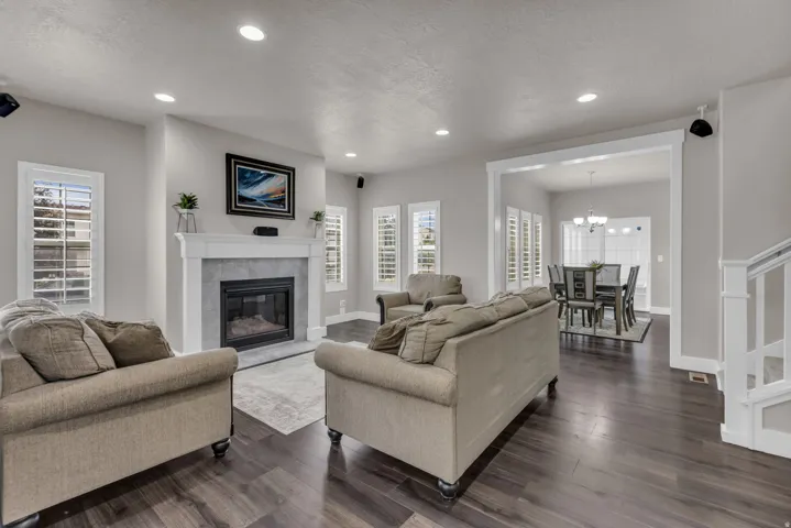 Spacious living area featuring wood-finish flooring, a tiled fireplace with a white mantel, recessed lighting, and plantation shutters