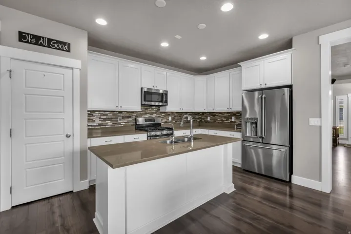 Kitchen featuring an island with an undermount sink, stainless steel appliances, recessed lighting, white cabinetry, and wood-finish flooring