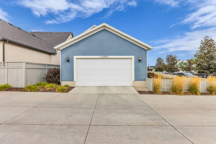 Attached two-car garage with a concrete driveway, complemented by exterior sconce lighting and surrounding landscaping