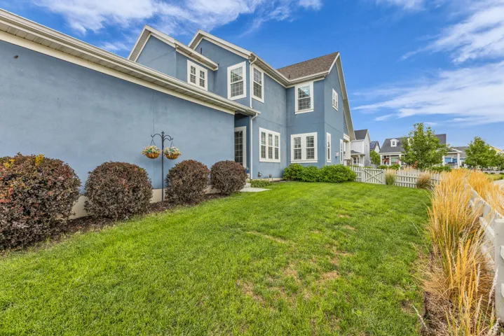 Exterior featuring a blue stucco finish, white trim, multiple windows, a sloped roof, and a green lawn