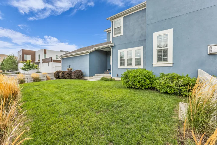 Exterior featuring blue stucco siding, white trim windows, a covered entry, and a green lawn with landscaping